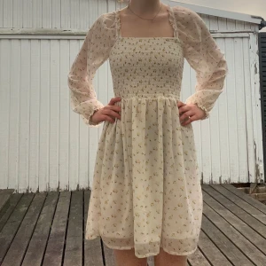 Ljus blommig kortklänning med puffärmar - Supersöt ljus kortklänning med små blommor, smockad överdel. Ärmar med genomskinlig tyg och blommor