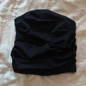 Svart bandeau tubtopp från NA-KD  - Säljer en svart bandeau tubtopp från NA-KD i storlek XS. Toppen har snygga draperade veck framtill som ger en cool och trendig look. Perfekt att styla med höga jeans eller kjol för en enkel men stilren outfit. Aldrig använd.