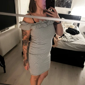 Randig offshoulder kortklänning - Snygg kort offshoulder-klänning med smala svarta och vita ränder. Klänningen har volang upptill och sitter tight mot kroppen. Aldrig använd 