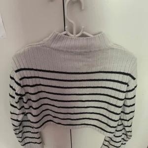 Randig croppad tröja från H&M - Säljer en croppad, ribbad tröja från H&M i vitt med svarta horisontella ränder. Tröjan har lång ärm, hög krage och är stickad i mjukt material. Perfekt för dig som gillar en chill och trendig stil.