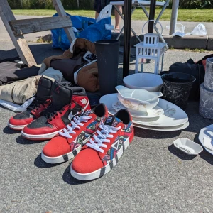 Nike Jordan 1 och röda sneakers/t-shirts/byxor m.m - Säljer ett par klassiska Nike Jordan 1 high sneakers i svart och rött skinn med vita detaljer och snörning. Medföljer även ett par röda sneakers med färgglatt geometriskt mönster, vita snören och platt sula. Perfekta för dig som vill sticka ut med coola skor.