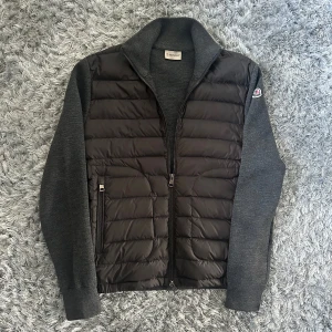 Grå hybridjacka från Moncler, S - Snygg grå hybridjacka från Moncler med quiltad, vadderad front i mörkgrått och stickade ärmar och rygg. Jackan har hög krage, två dragkedjefickor och Moncler-logga på ärmen. Perfekt för lager-på-lager och chill höst- eller vårstil.