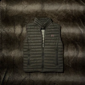 Grå Colmar dunväst  - Säljer denna snygga gråa dunväst från Colmar med dragkedja och hög krage. Västen har en diskret logga på bröstet. Perfekt för lager-på-lager. Skriv om ni undrar något 