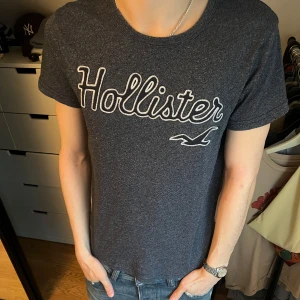 T-shirt från Hollister - Säljer en blå/grå t-shirt från Hollister med tryck. Den är i mycket bra skick och storleken är XS.