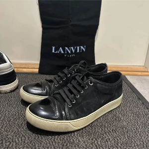Svarta sneakers från Lanvin - Snygga svarta sneakers från Lanvin med en stilren design. Skorna har en svart ovandel med snörning och en kontrasterande vit sula. Perfekta för en casual look.