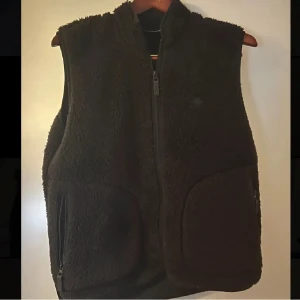 Svart fleeceväst från J.Lindeberg - Säljer en svart fleeceväst från J.Lindeberg. Nypris ungefär 1400kr, köpt i butik på J.Lindebeg. Västen har en dragkedja framtill och två praktiska fickor med dragkedjor. Skick 9/10 knappast använd. Strl L men passar M också!