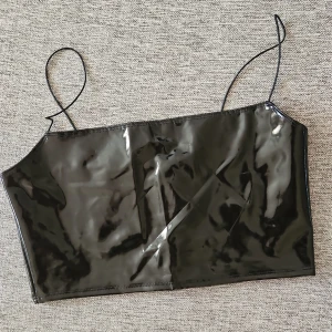 Svart glansig topp - Snygg svart glansig topp med tunna axelband. Perfekt för en kväll ute eller en speciell tillställning. Den har en stilren och modern look som verkligen sticker ut.