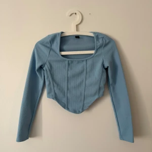 Ljusblå långärmad topp - Säljer en stilren ljusblå topp med lång ärm och fyrkantig halsringning. Toppen har en figurnära passform och är perfekt för både vardag och festliga tillfällen. Den är tillverkad i ett mjukt och bekvämt material. Möts upp i Stockholm 📍 fraktar inte! 