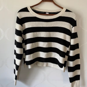 Svartvit randig stickad tröja - Säljer en snygg svartvit randig stickad tröja med långa ärmar. Tröjan har en croppad passform och ribbade kanter vid ärmslut och nederkant. Perfekt för en stilren look!