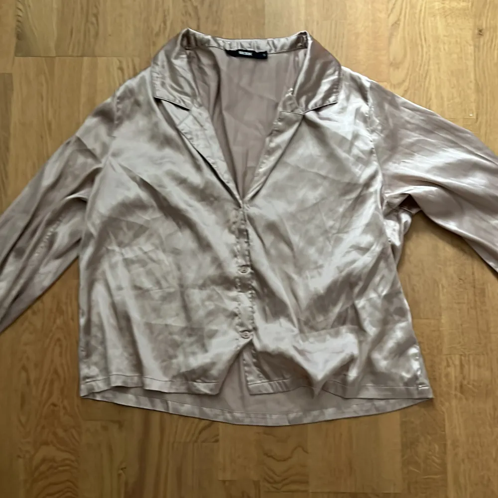 Snygg beige pyjamas blus i siden från Bik Bok. Blusen har långa ärmar och knappar framtill. Perfekt för en elegant look.. Puserot.