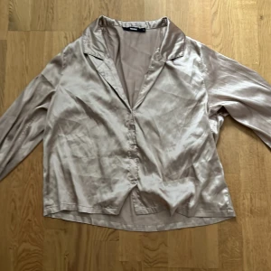 Beige pyjamas blus från Bik Bok - Snygg beige pyjamas blus i siden från Bik Bok. Blusen har långa ärmar och knappar framtill. Perfekt för en elegant look.