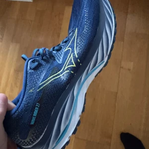 Blå löparskor från Mizuno - Säljer ett par blå Mizuno Wave Rider 27 löparskor med snygga gula detaljer och snörning. Skorna har en bekväm sula som ger bra stöd under löpningen. Perfekta för dig som älskar att springa och vill ha stilrena skor.