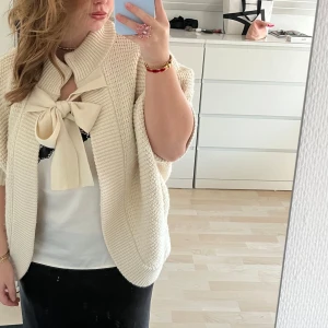 Stickad kofta  - Säljer en mysig vit stickad kofta med korta ärmar och en stor dekorativ rosett framtill. Perfekt för att lägga till en elegant touch till din outfit. Passar bra till både vardag och speciella tillfällen.💞PRIS GÅR ATT DISKUTERA VID SNABBAFFÄR💞