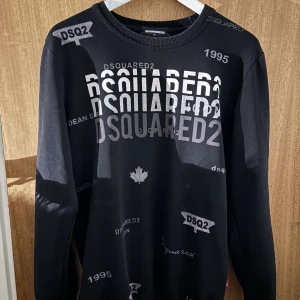 Svart långärmad tröja från Dsquared2 - Snygg svart långärmad tröja från Dsquared2 med flera tryck av märkesnamnet i olika storlekar och stilar. Perfekt för en stilren och modern look. Tröjan har en rund halsringning och är tillverkad i ett mjukt material.