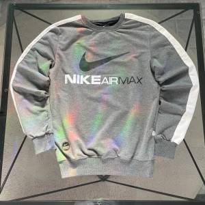 Grå Nike Air Max sweatshirt - Säljer en grå Nike Air Max sweatshirt med regnbågseffekt. Tröjan har vita ränder längs ärmarna och ett stort Nike Air Max-tryck på framsidan. Perfekt för en sportig look!