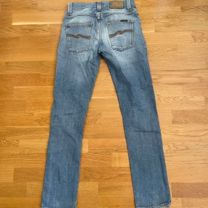 Nudie jeans - Snygga blå jeans från Nudie Jeans med slitna detaljer på knäna. De har en klassisk femficksdesign och en knappgylf. Perfekta för en avslappnad stil.