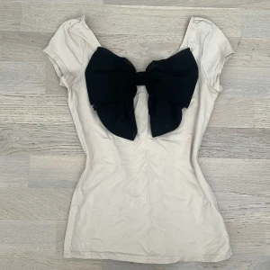 Vit topp med  svart roset - Säljer en söt vit topp från H&M Divided med en stor svart rosett framtill. Toppen har korta ärmar och en rund halsringning. Perfekt för att ge en outfit en extra touch! 🖤