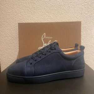 Mörkblå sneakers från Christian Louboutin - Snygga mörkblå sneakers från Christian Louboutin med klassisk röd sula. Skorna har en stilren design med snörning och är tillverkade i ett elegant material som ger en lyxig känsla.