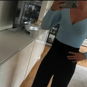 Ljusblå ribbad omlottopp - Säljer en stilren ljusblå omlottopp med ribbad struktur. Toppen har långa ärmar och en croppad passform som ger en modern look. Perfekt för att lyfta din outfit! Använd en gång 