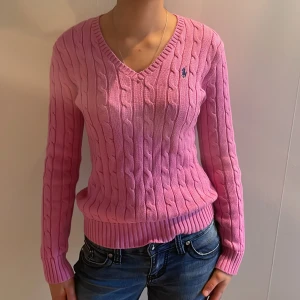 Rosa stickad tröja från Ralph Lauren - Säljer en snygg rosa stickad tröja från Ralph Lauren som är äkta med kabelstickat mönster och v-ringning. Tröjan har långa ärmar och en liten broderad logga på bröstet. säljer pga inte användning men tycker den är jätte fin och jätte skön💓. Passar till vardags!💓🤩