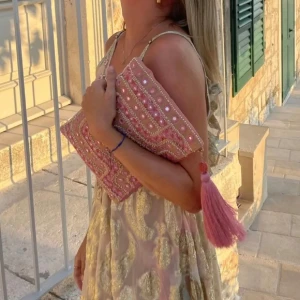IBIZA style clutch - SLUTSÅLD Säljer en superfin rosa kuvertväska med detaljerat broderi och en stor tofs. Väskan har ett unikt mönster i rosa och guld med små speglar och pärlor. Perfekt för att ge en färgklick till din outfit! Pärlor, paljetter, rosa, från Indiska, nypris 350kr, nyskick, väska, necessär, glitter, sequins, sommar, sthlm