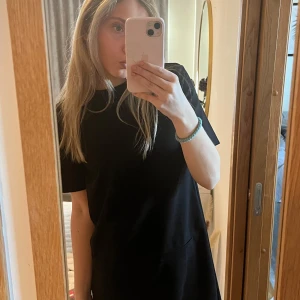 Svart klänning - Säljer en stilren svart klänning med korta ärmar. Perfekt för en minimalistisk look. Klänningen har en enkel design med två fakefickor framtill.