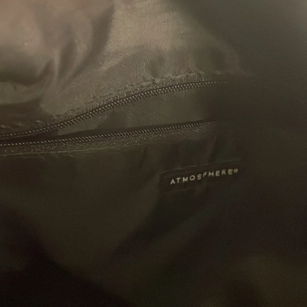 Snygg svart handväska från Atmosphere med flätad detalj på framsidan. Väskan har två handtag och en dragkedja upptill. Perfekt för att bära dina dagliga nödvändigheter med stil.. Laukut & Käsilaukut.