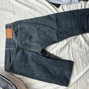 Levis 501 jeans - Klassiska Levis 501 jeans i mörkblå denim med en rak passform. De har en traditionell femficksdesign och en knappgylf. Perfekta för en tidlös stil.