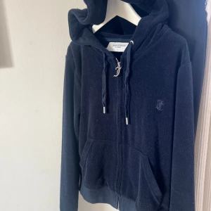 Mörkblå kofta från Juicy Couture - Säljer en mörkblå kofta från Juicy Couture med dragkedja och huva. Tröjan har långa ärmar och en broderad logga på bröstet. Koftan är i frottématerial. 