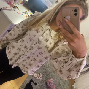 Gullig blus med röda blommor och krage - En söt gullig blus med mörk röda blom buketter på, tröjan har ganska puffiga armar, bruna små knappar, det finns knappar vid handen/armen också. Det är storlek S men den är ju lite större. Blusen/koftan är ifrån Kappahl (Newbie märket i Kappahl) tröjan har också en krage med lite spets❤️