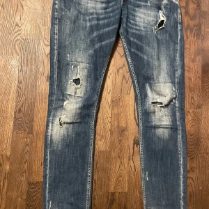 Blåa dondups! - Säljer ett par blå jeans med slitningar och hål på framsidan. De har en klassisk femficksdesign och en snygg tvättad look. Perfekta för en avslappnad stil.