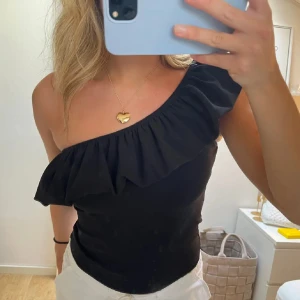 Topp med volang  - Jättefin one-shoulder topp med volang. Sitter fint på och är materialet är lite stretchigt. Knappt använd och i fint skick.