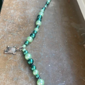 Grönt pärlhalsband med sköldpaddshänge - Charmigt halsband med gröna pärlor i olika nyanser och ett unikt sköldpaddshänge. Perfekt för att ge en färgglad touch till din outfit.