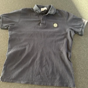 Mörkblå pikétröja från Stone Island Junior - Snygg mörkblå pikétröja från Stone Island Junior med klassisk krage och knappslå. Tröjan har en broderad logotyp på bröstet som ger en stilren look. Perfekt för en avslappnad stil.