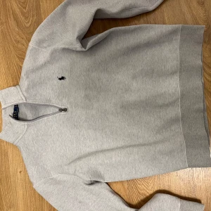 Ralph lauren sweatshirt - Säljer en stilren grå tröja från Polo Ralph Lauren med dragkedja vid halsen och det klassiska logotypbroderiet på bröstet. Perfekt för en avslappnad och snygg look.