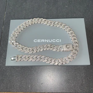 Iced halsband från Cernucci - Säljer ett glittrigt halsband från Cernucci. Halsbandet har en robust kedjedesign med en skinande yta som ger ett lyxigt intryck. Perfekt för att ge en extra touch av glamour till din stil.