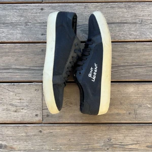 Svarta sneakers från Saint Laurent - Snygga svarta sneakers från Saint Laurent med vit sula och märkets namn tryckt på sidan. Skorna har snörning och kommer med originalförpackning och dustbag. Pris kan diskuters 