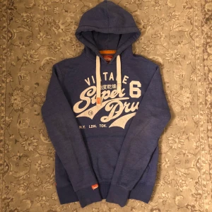 Blå Superdry Hoodie - Säljer nu denna fräscha Blåa Superdry hoodie med vita detaljer| den är i väldigt bra skick skulle säga runt 9/10 bara lite använd| Storlek S och passar som det också, Vid frågor eller funderingar är det bara att höra av sig🙌
