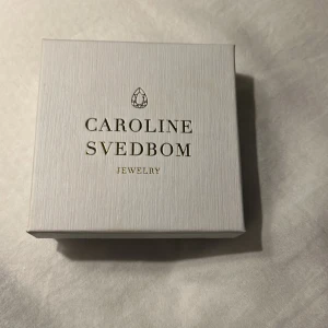 Guldarmband från Caroline Svedbom - Elegant guldarmband från Caroline Svedbom med en vriden design och två klara kristaller i ändarna. Perfekt för att lägga till en touch av glamour till din outfit.