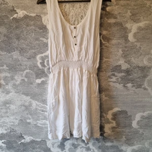 Vit klänning från Amisu - Vit klänning från Amisu med spetsdetaljer och knappar framtill i bohostil. Klänningen är i mycket bra skick. Jag hittar ingenting att anmärka på.