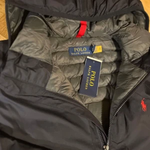 Svart dunjacka från Polo Ralph Lauren - Säljer en stilren svart dunjacka från Polo Ralph Lauren. Jackan har en praktisk huva och dragkedja framtill. Den är lätt och packbar, perfekt för kyliga vår/höst dagar. Ord pris: 4295:-   Hör av dig om du har mer frågor mvh 
