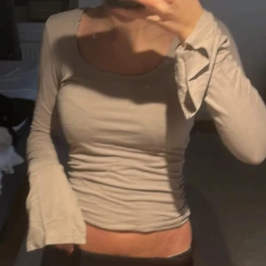 Beige långärmad topp med slits  - Säljer en beige långärmad topp med en snygg slits vid ärmen. Toppen har en tight passform och är perfekt för en stilren look. Passar bra till både jeans och kjol.