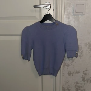 Ljuslila tröja från Zara - Säljer en söt ljuslila tröja från Zara med korta ärmar och dekorativa knappar på axeln och ärmsluten. Perfekt för en stilren look. 💜