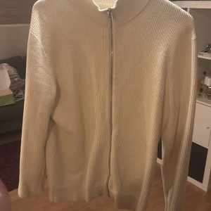 Vit ribbad tröja från East West - Säljer en stilren vit ribbad tröja från East West med dragkedja framtill. Tröjan har långa ärmar och en hög krage, perfekt för kyligare dagar. Passar bra till både jeans och chinos.