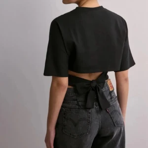 Svart croppad topp med knyt - Snygg svart croppad topp med korta ärmar och knytning i ryggen. Perfekt för en stilren look. Aldrig använd. 