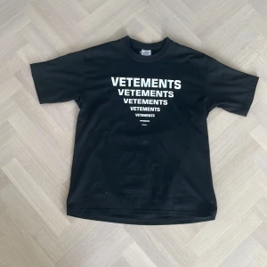 Svart t-shirt från Vetements - Säljer en svart t-shirt från Vetements med tryck i vitt på både fram- och baksidan. T-shirten är unisex och tillverkad i 100% bomull, vilket gör den både bekväm och stilren. Köptes på Vinted förra sommaren för 1500, oklar om äkthet men den e riktigt snygg och passar dig som söker en alternativ stil! Priset kan diskuteras.