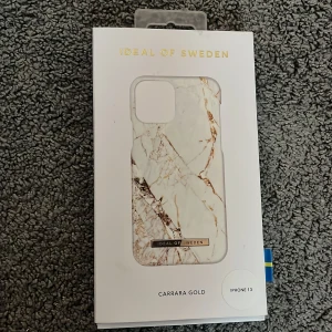 Carrara Gold mobilskal från Ideal of Sweden - Snyggt mobilskal för iPhone 13 från Ideal of Sweden i mönstret Carrara Gold. Skalet har en elegant marmordesign med inslag av guld och är både stilrent och skyddande. Perfekt för att ge din telefon en lyxig touch. Helt nytt oanvänd