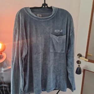 Blå velourtröja från Polar - Säljer en mjuk och bekväm blå velourtröja från Polar. Tröjan har ett diskret randigt mönster och en praktisk bröstficka. Den har långa ärmar och en elastisk nederkant för en avslappnad passform. Perfekt för kyliga dagar!