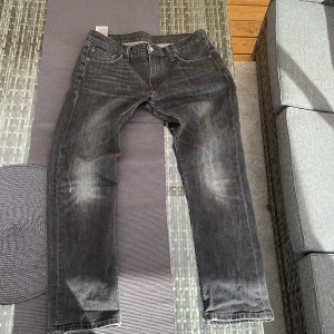 Svart fadeade jeans från Levis - Säljer ett par svarta Levis jeans med en klassisk femficksdesign. Jeansen har en straight passform och är tillverkade i slitstarkt denim. Perfekta för en avslappnad stil. 