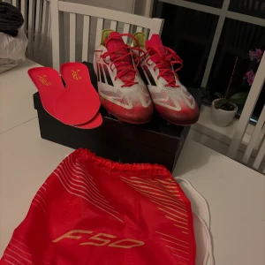 Adidas F50 fotbollsskor - Säljer ett par Adidas F50 fotbollsskor i vitt med svarta och röda. Perfekta för fotbollsplanen med sin lätta design och greppvänliga sula.